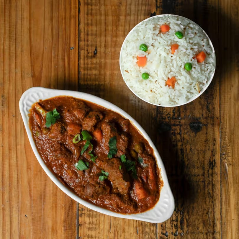 Indian lamb curry with rice, peas, and carrots on a rustic wooden table.