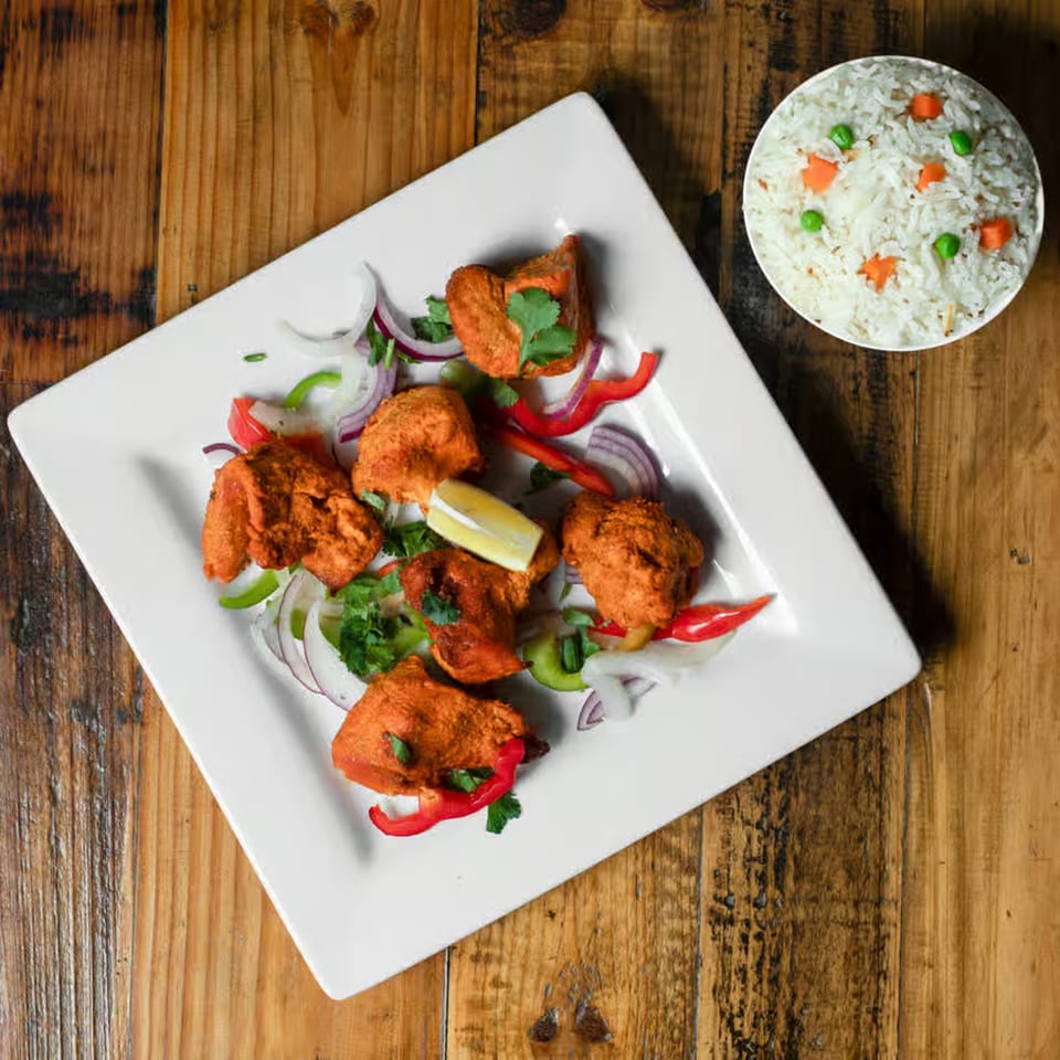 Indian chicken tikka with onions, peppers, cilantro, and lemon, served with a side of rice.