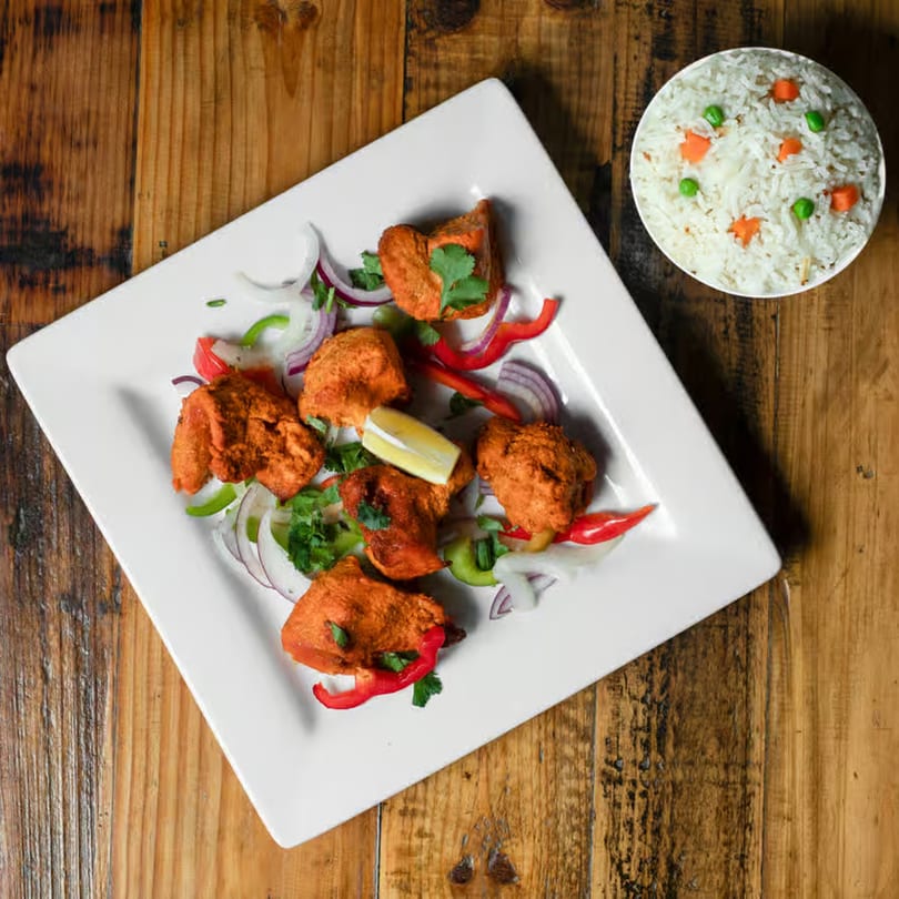 Indian chicken tikka with onions, peppers, cilantro, and lemon, served with a side of rice.
