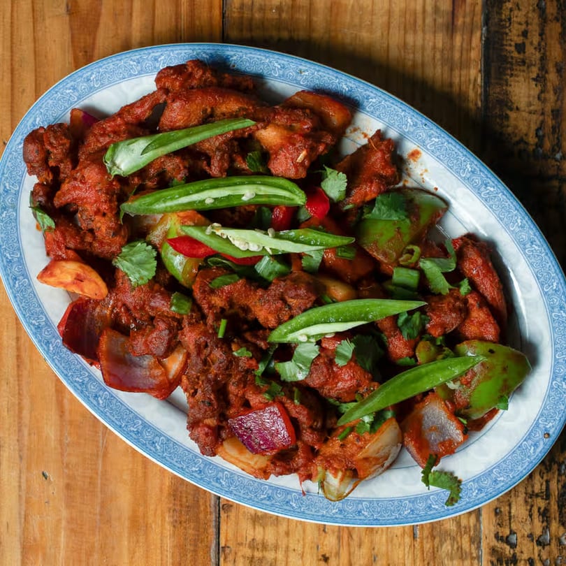 Spicy Indian chicken chili with bell peppers, onions, and cilantro on a white and blue platter.